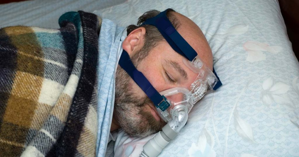 Man with beard sleeping with CPAP mask