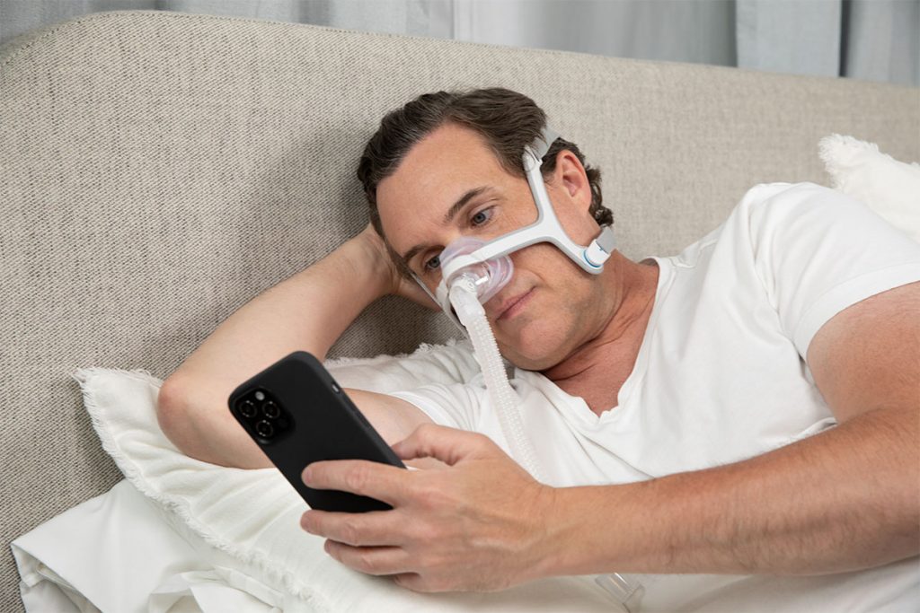 man lounging in bed on his phone wearing airfit n20 cpap mask