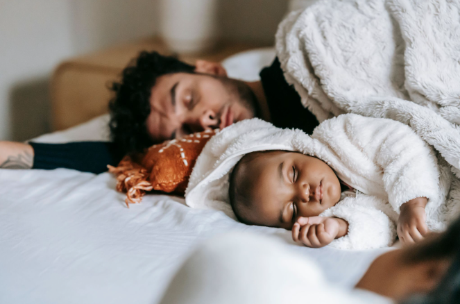 A father and baby sleep peacefully side by side on a bed.
