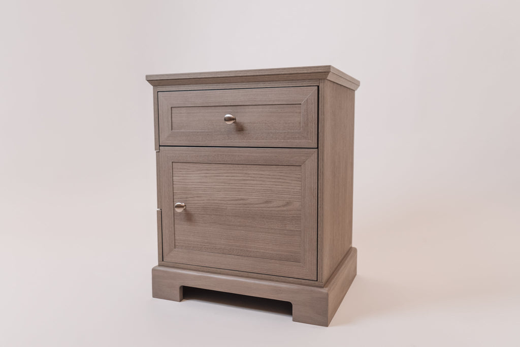 A three-quarter angled view of the Charleston Gray CPAP nightstand, emphasizing its elegant wood grain finish, structured base, and functional design. The top drawer and lower cabinet door, both with metallic knobs, add to its sophisticated look.