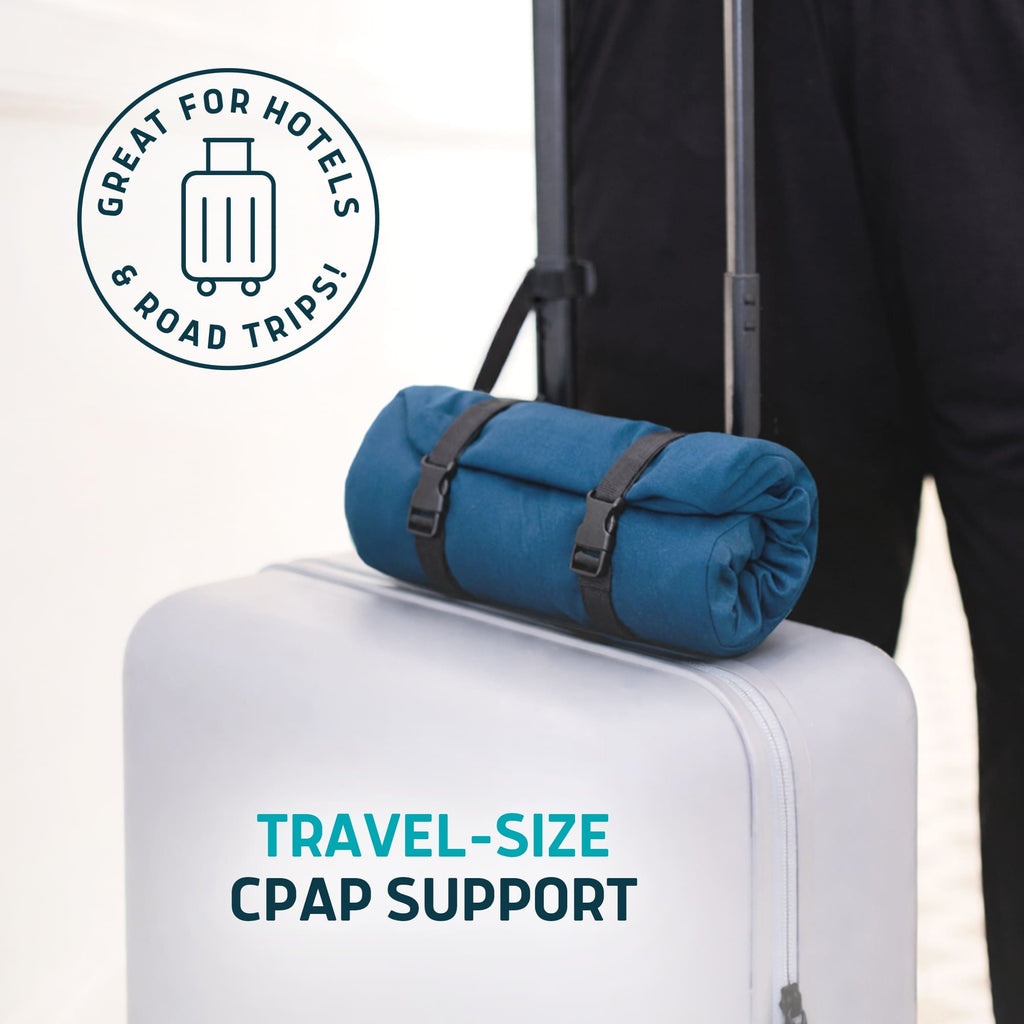 Blue rolled-up Lunderg travel CPAP pillow secured with straps on top of a white suitcase.