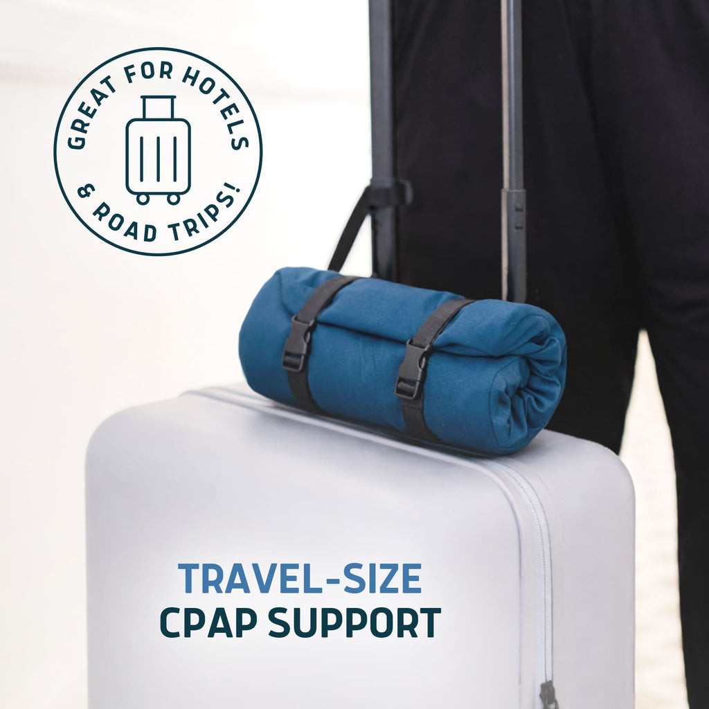 Blue Lunderg travel CPAP pillow rolled up and strapped to the handle of a white suitcase.