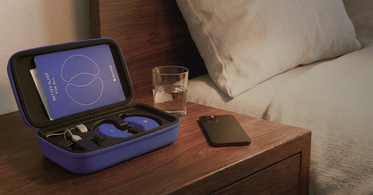 Blue Wesper sleep headset in an open charging case on a wooden bedside table next to a phone and water.