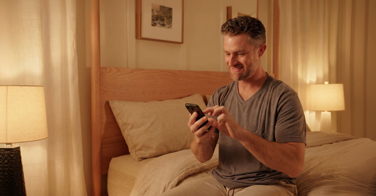 A smiling man sitting in bed using a smartphone.