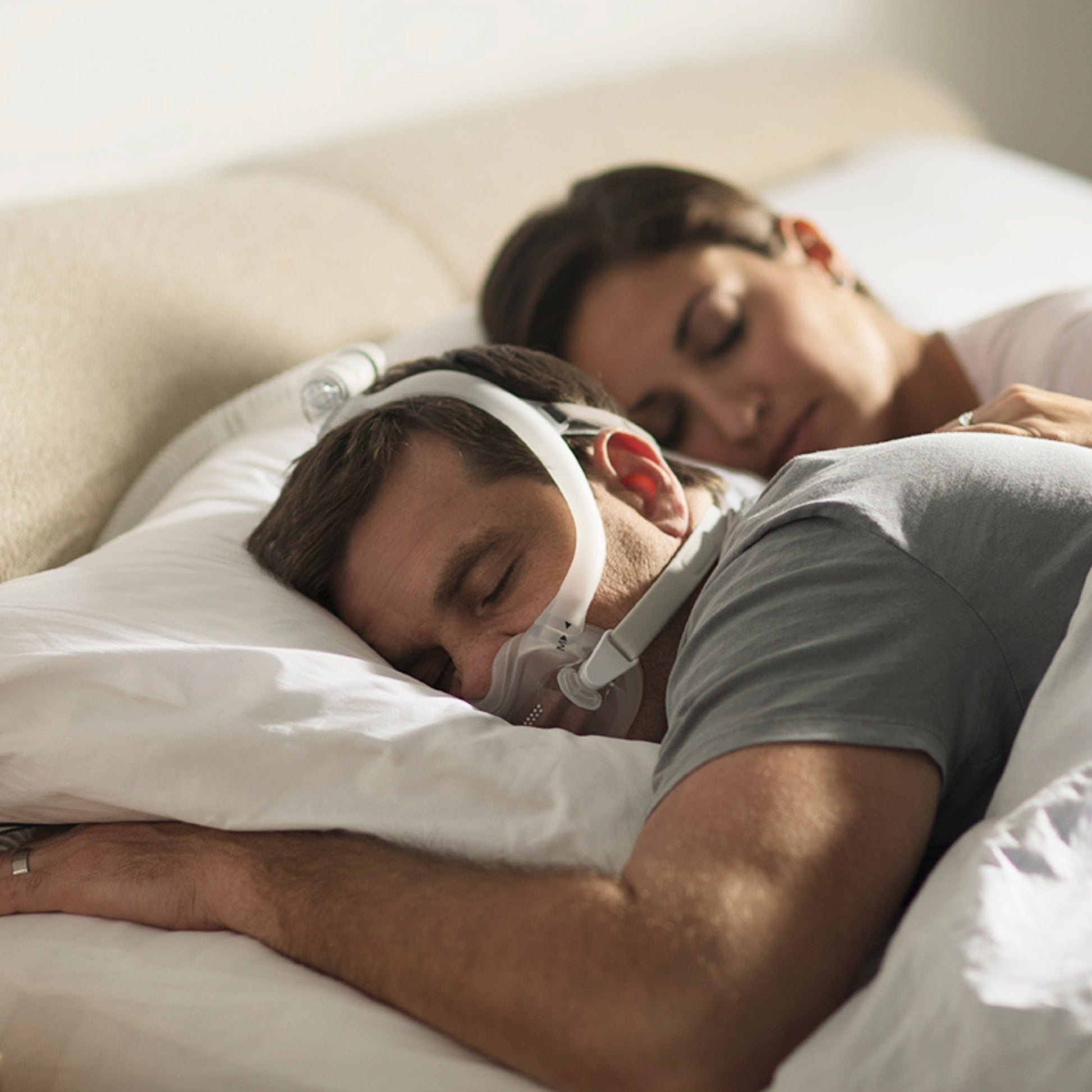 Man sleeping soundly on his side while wearing the dreamwear full face mask, with his partner sleeping behind him