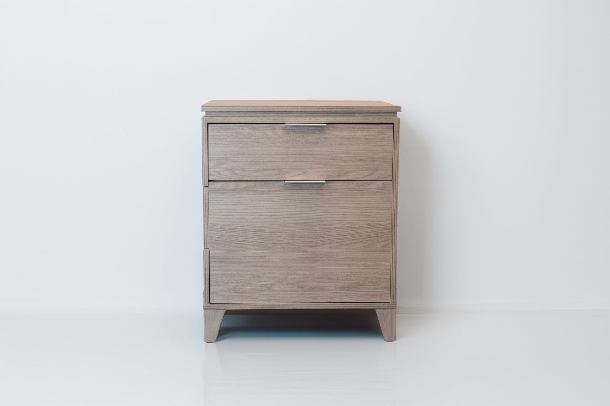 A full front-facing view of the Soho Grey CPAP nightstand, showcasing its clean lines, smooth wood grain finish, and modern metal handles. The nightstand stands on tapered legs, adding to its stylish and practical appeal.