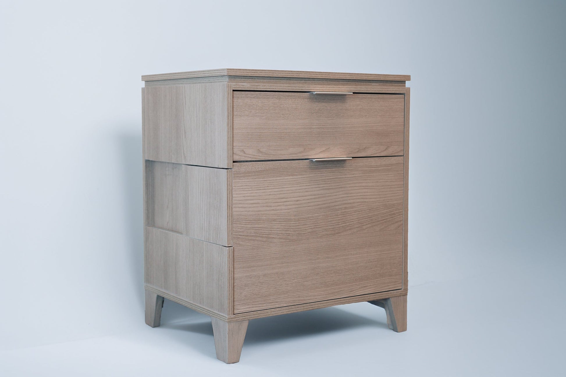 A CPAP nightstand in Soho Grey finish with a modern, minimalist design. The nightstand features two drawers with sleek metal handles, side cutouts for easy access, and slightly tapered legs for a contemporary look.