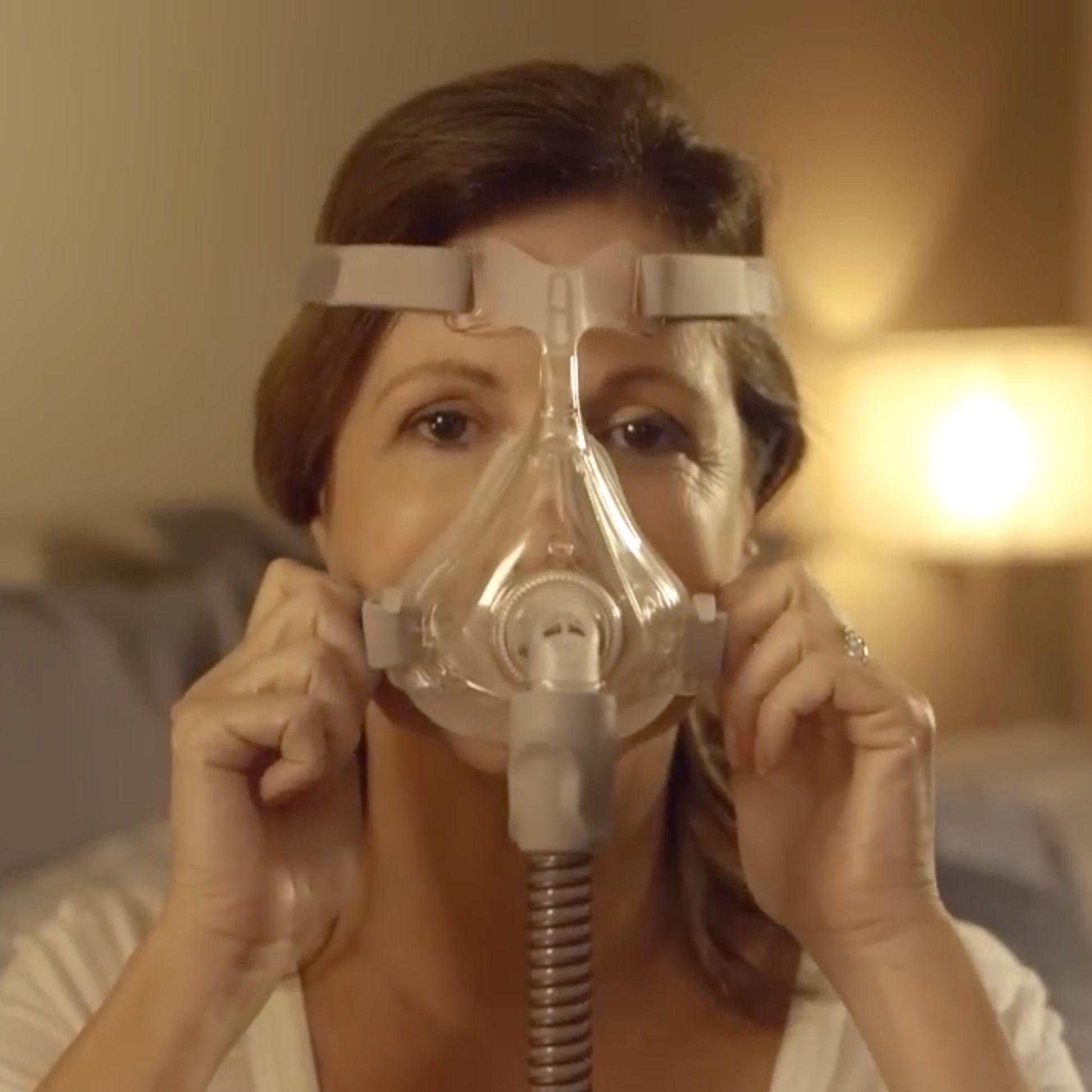 Front-facing image of a woman adjusting a  Quattro™ Air Full Face Mask with Headgear  For Her on her face