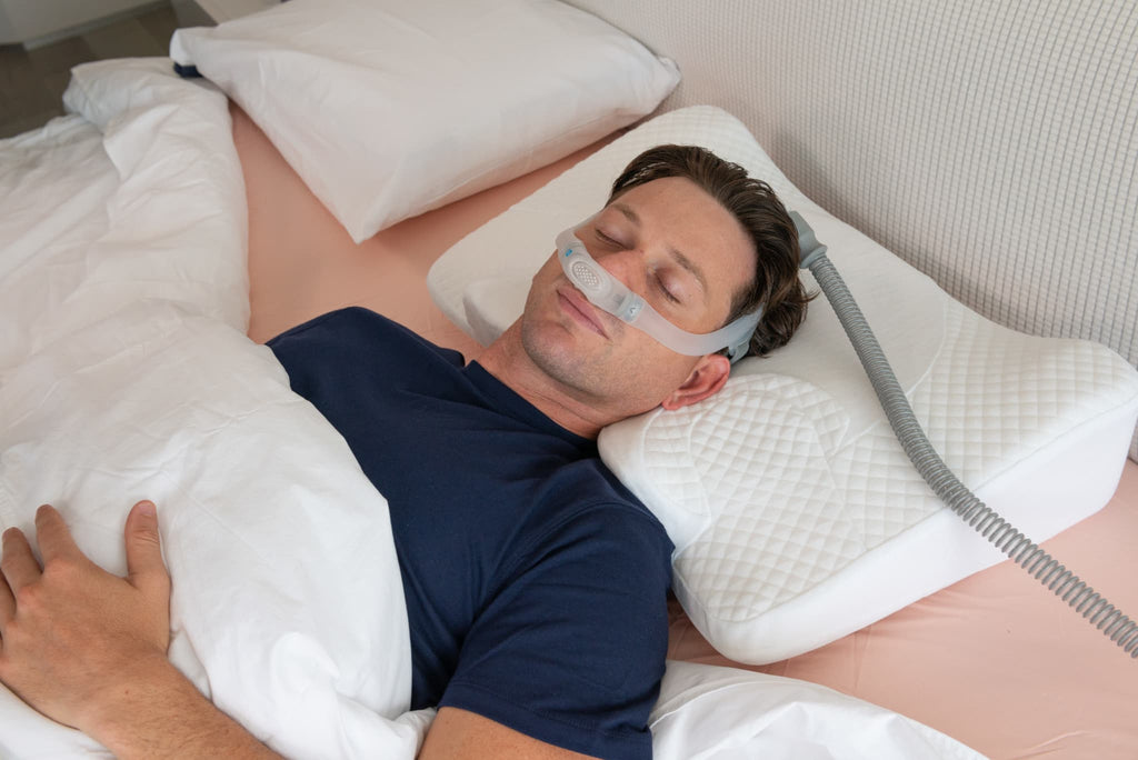Man sleeping comfortably with Snugell Memory Foam CPAP Pillow, supporting CPAP mask and tubing for optimal comfort.