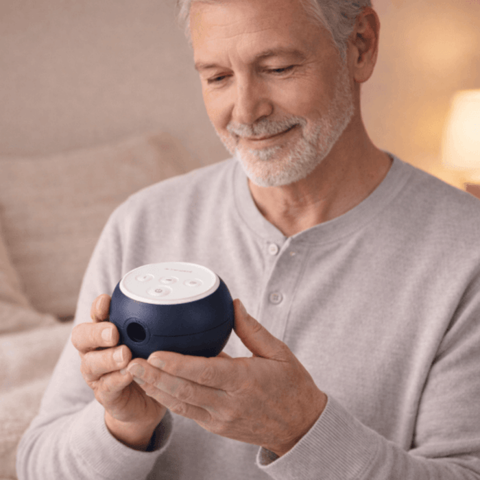 An older man holding a compact, navy blue Transcend Micro 510 travel CPAP machine in his hands.